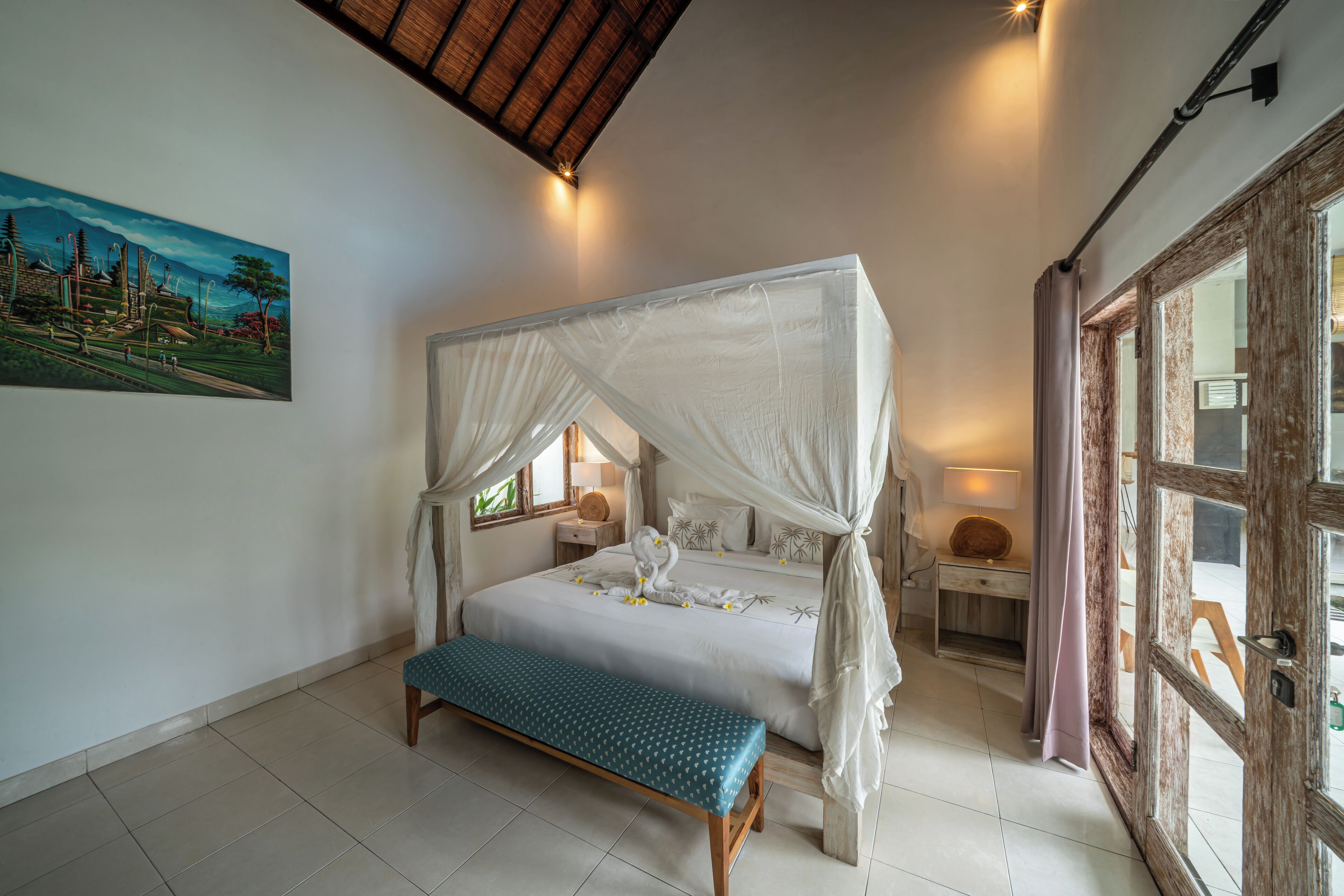 A bedroom with a four-poster bed, a bench, bedside tables, and a painting on the wall.