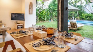 A dining table set with plates, glasses, and cutlery, with a view of a pool and greenery outside.