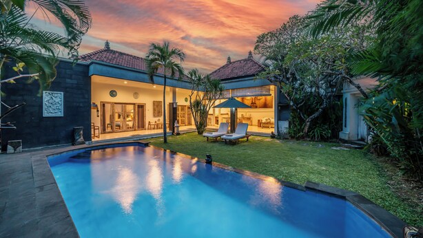 A modern house with a swimming pool, a well-maintained lawn, and a patio area with lounge chairs.