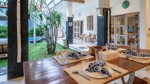 A dining table set with plates, glasses, and cutlery, with a view of a garden and outdoor seating area.