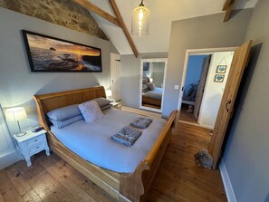 A bedroom with a wooden bed, a nightstand, a lamp, a painting, and a mirror. - 3 Double Bed Character Cottage in Quiet Hamlet (Tregoodwell)