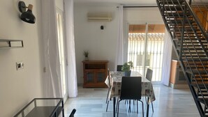 A dining area with a table, chairs, and a potted plant. There is a staircase on the right and a door with a curtain on the left. - 1029 Casa Evelyn C (Nerja)