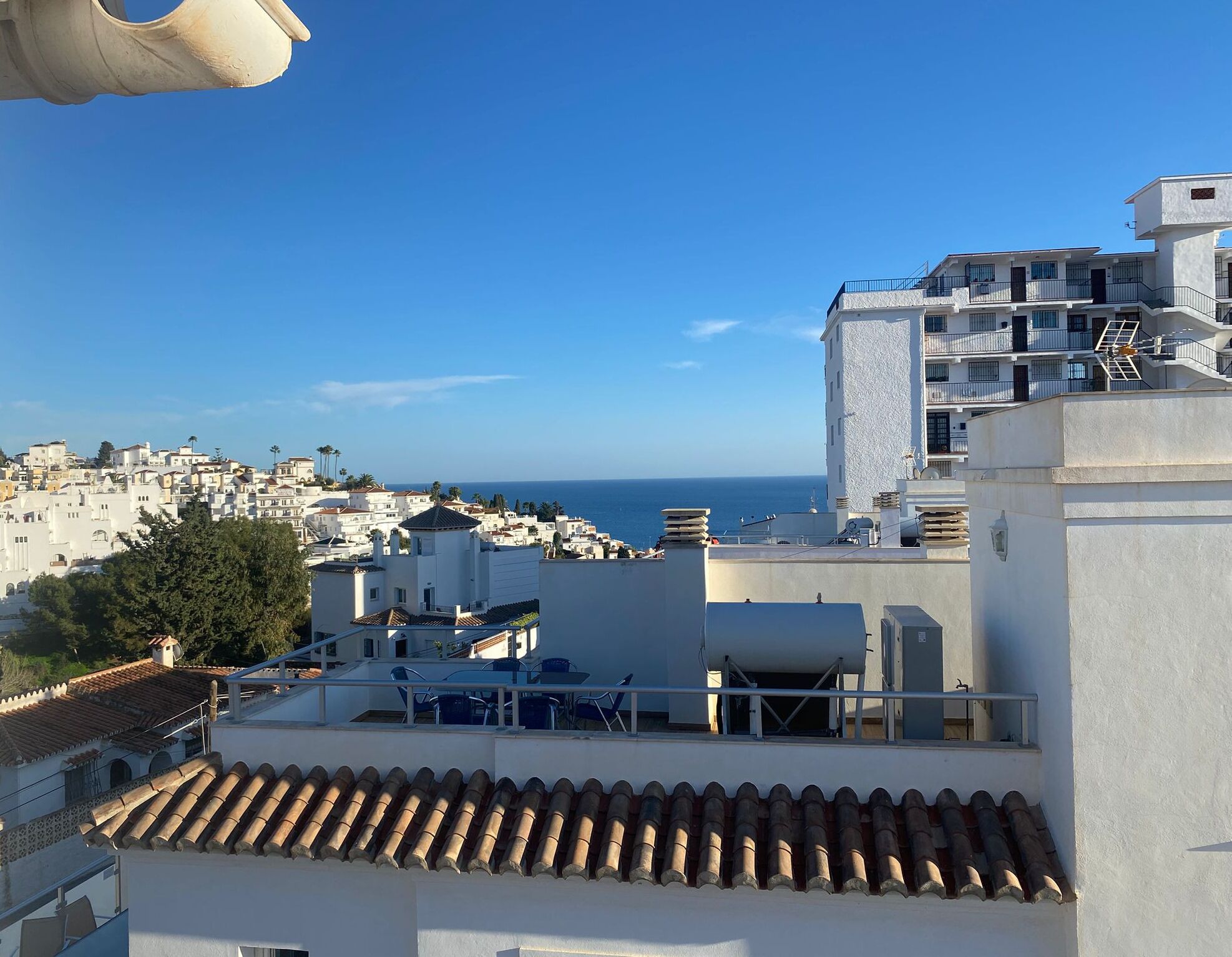 Una zona residenziale costiera con edifici bianchi, un cielo blu limpido e vista sul mare.