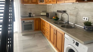 A modern kitchen with wooden cabinets, stainless steel appliances, a sink, and a built-in washing machine. - 1029 Casa Evelyn C (Nerja)