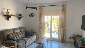 A living room with a sofa, a coffee table, a TV, and a window with curtains. - 1029 Casa Evelyn C (Nerja)