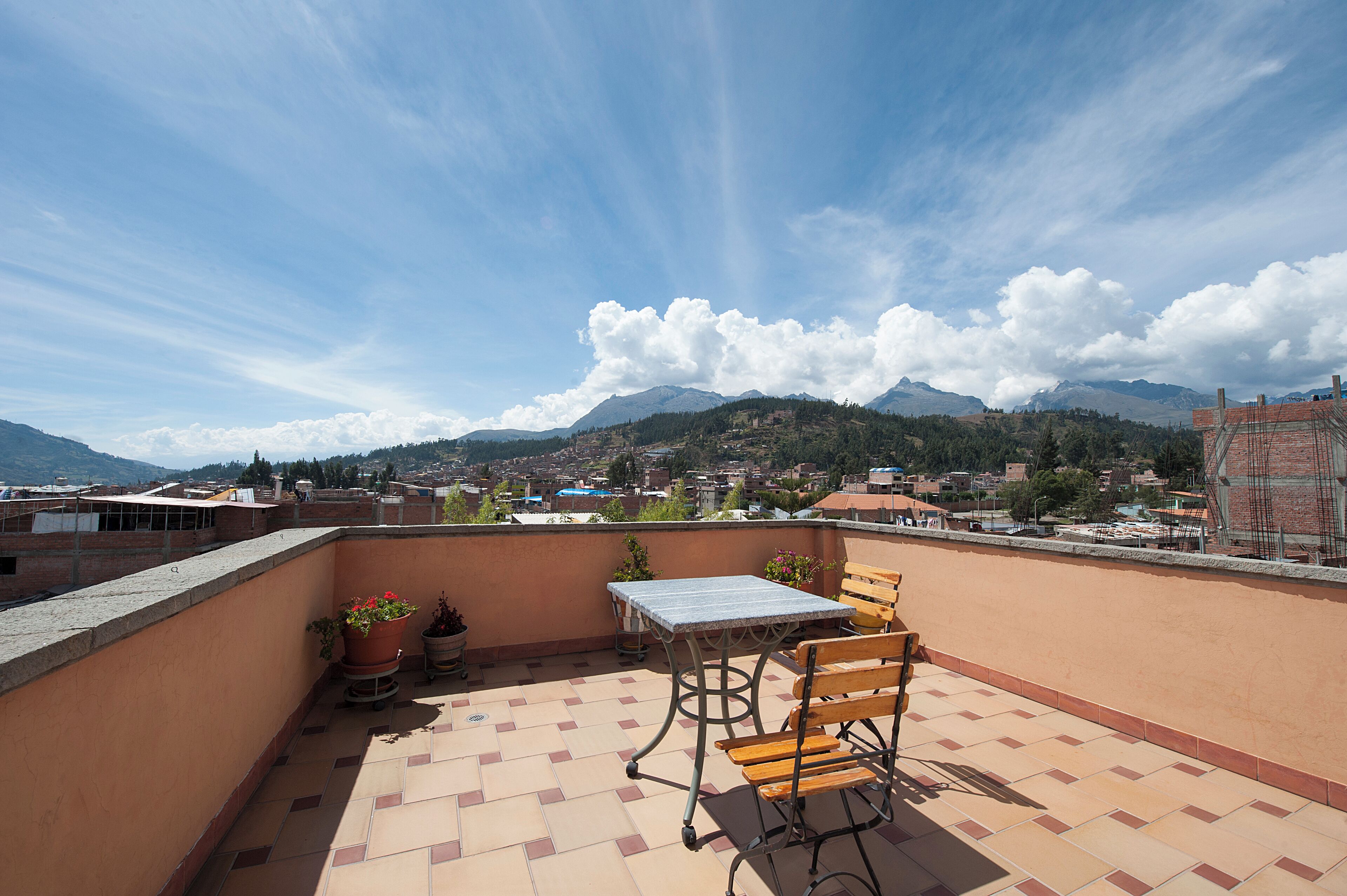 Una terraza en la azotea con mesa y sillas, plantas en macetas y vistas a un pueblo y montañas.