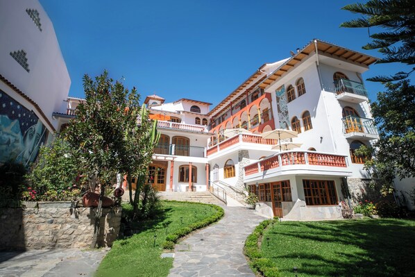 Un edificio de varios pisos con un patio central, sendero de piedra y abundante vegetación.