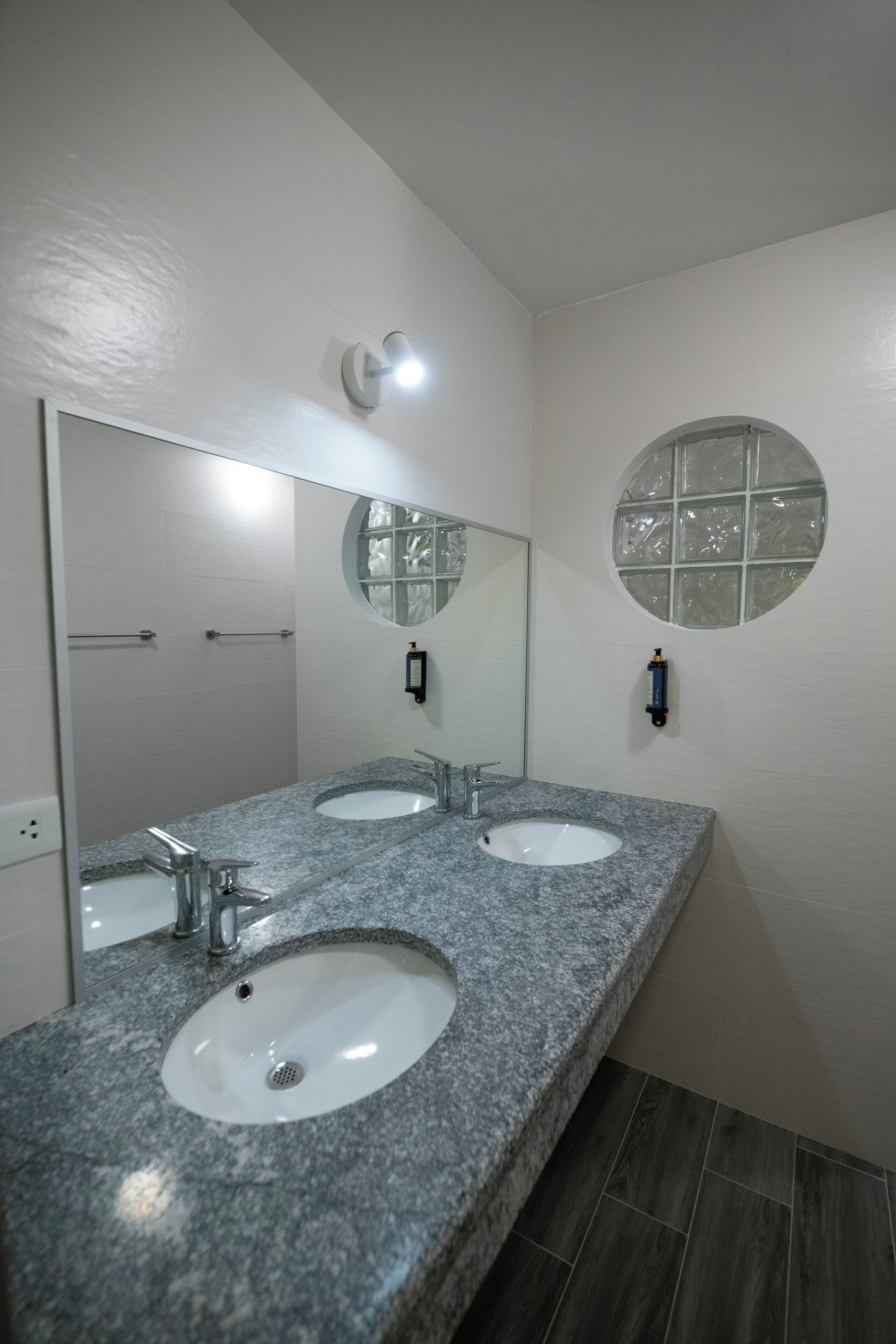 Un baño con dos lavamanos, un espejo grande y un ventanal redondo.