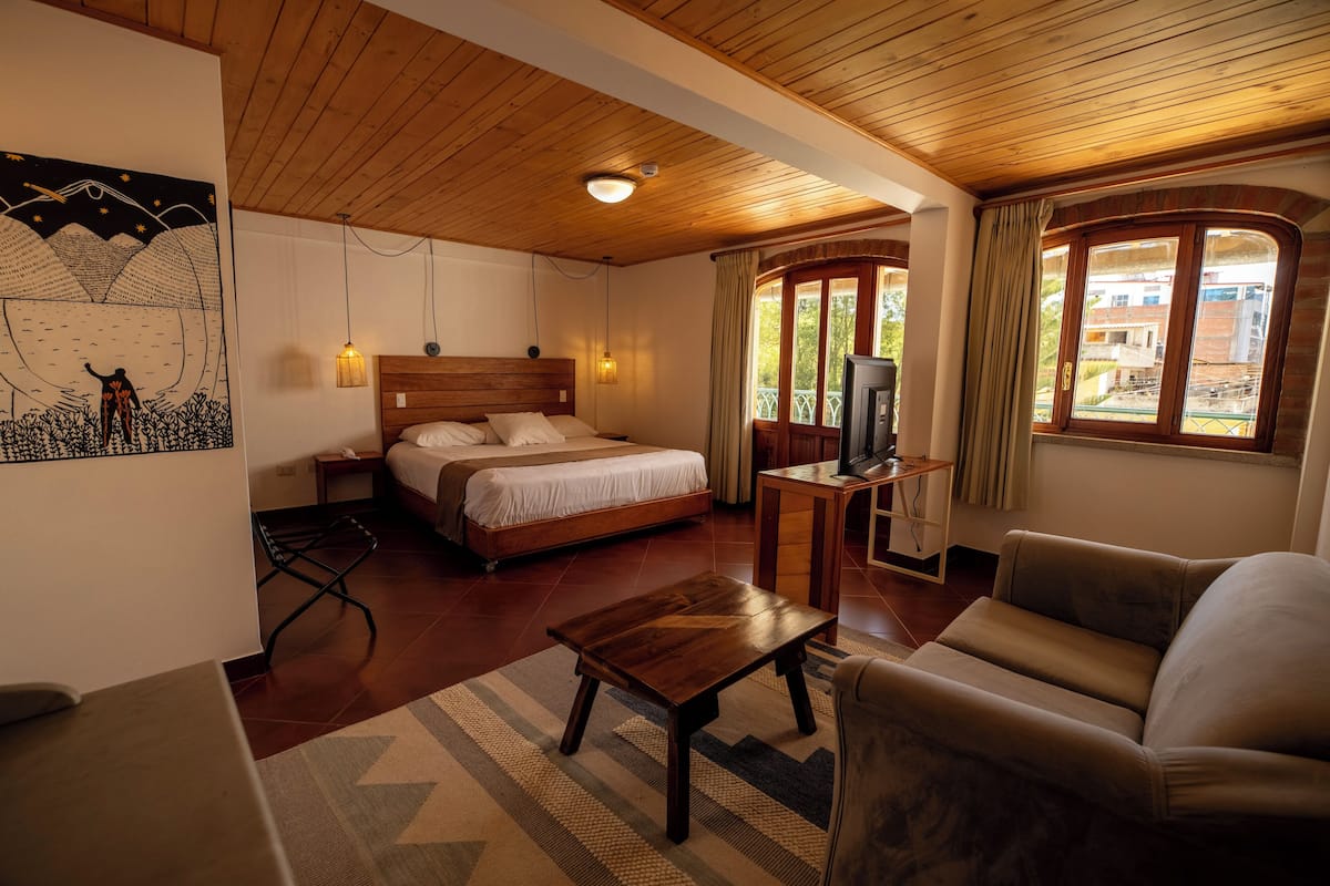 Un dormitorio con techo de madera, cama, televisor y ventana con cortinas.