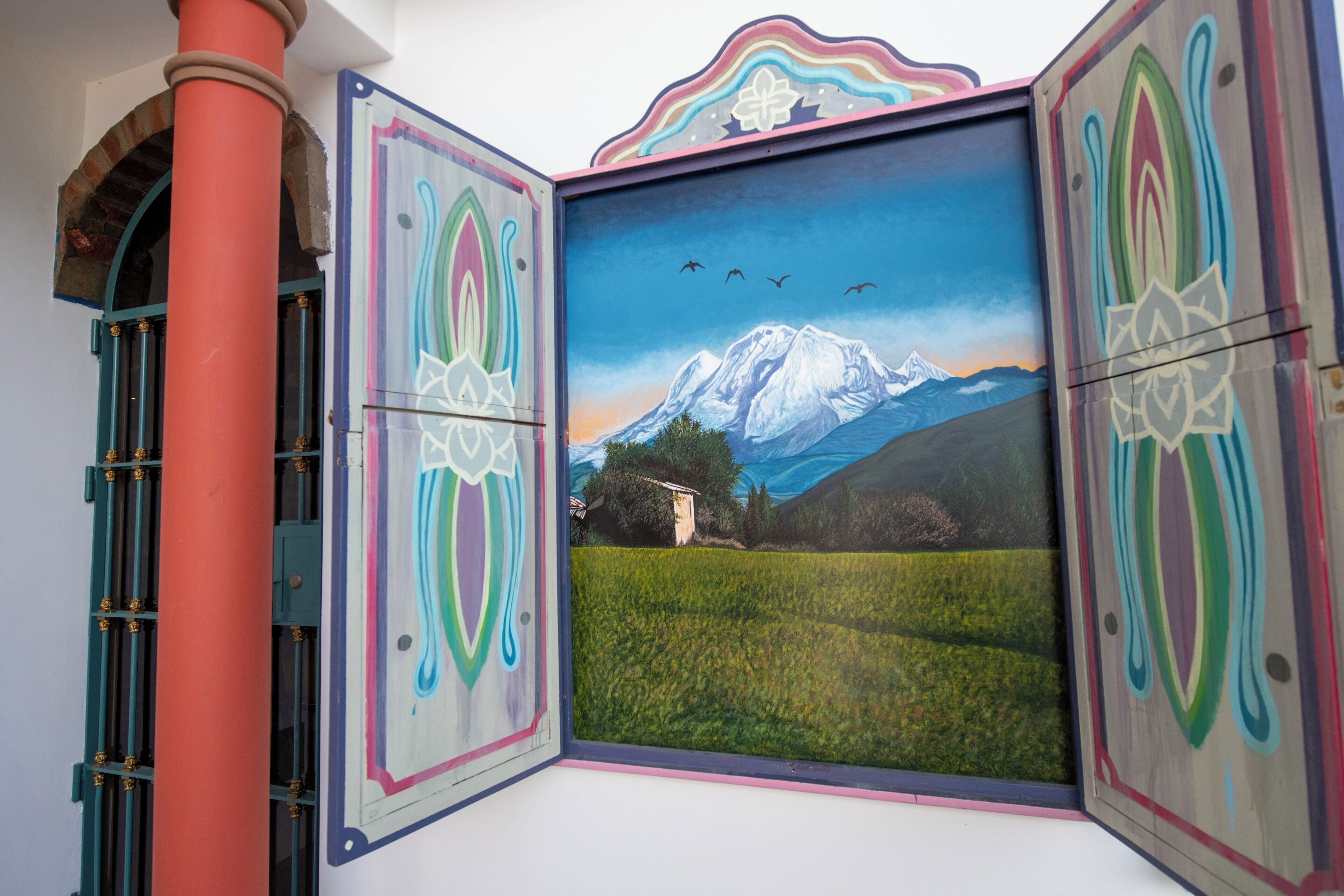A framed painting of a mountain landscape with birds, a house, and a field.
