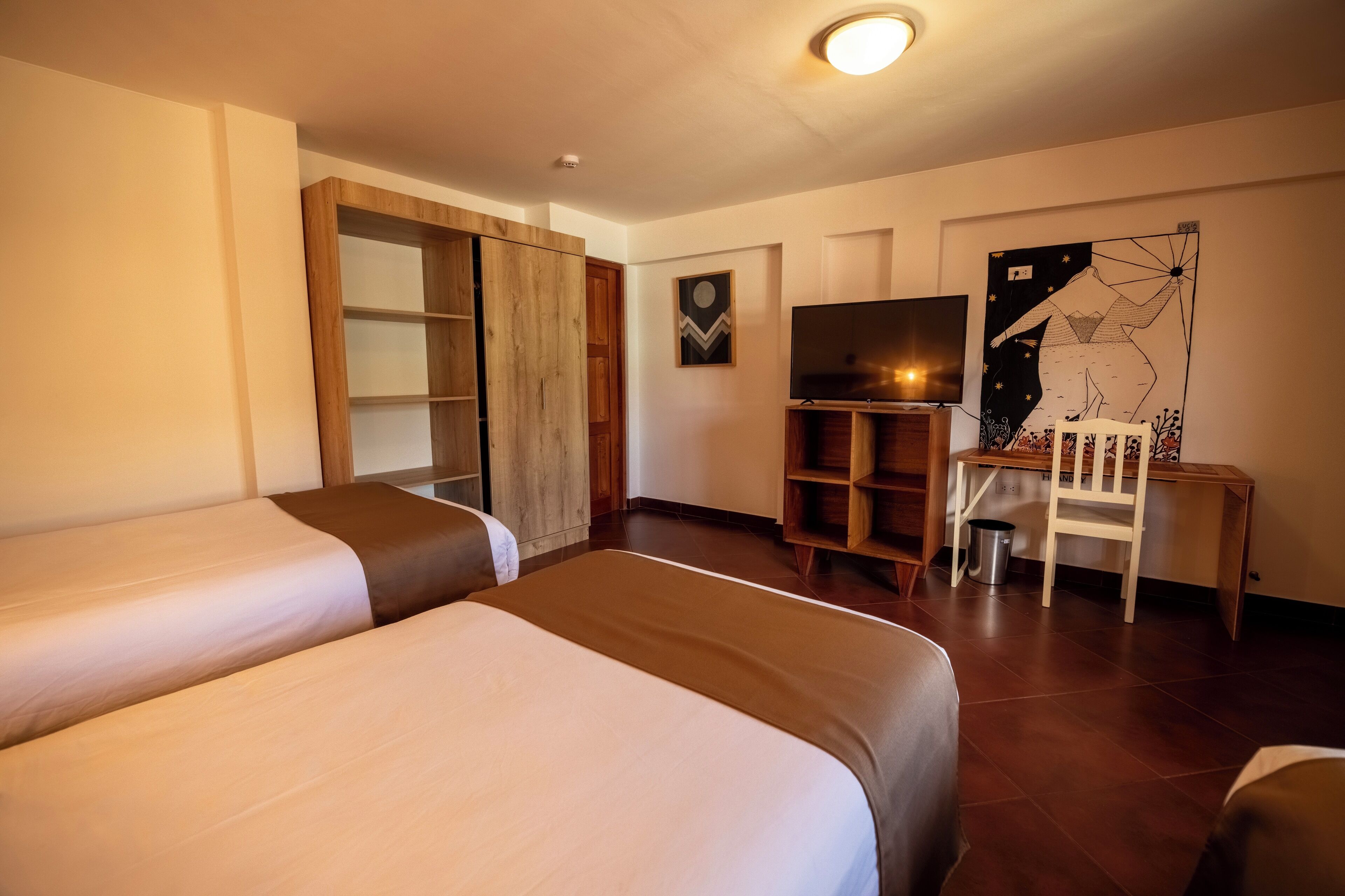 Quarto de hotel com duas camas, televisão, escrivaninha e uma cadeira.