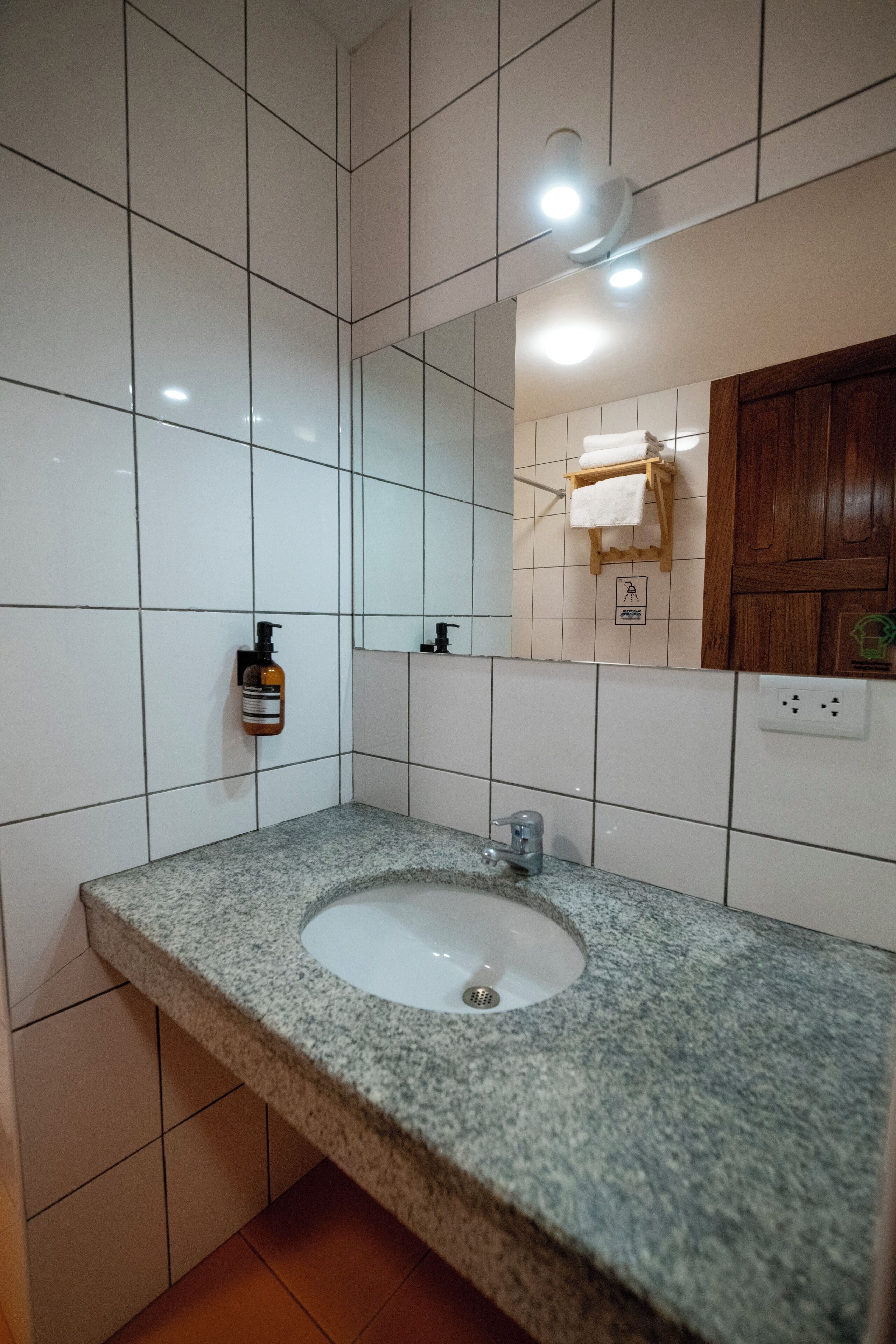 A bathroom with a granite countertop sink, white tiled walls, a mirror, a towel rack, and a soap dispenser.