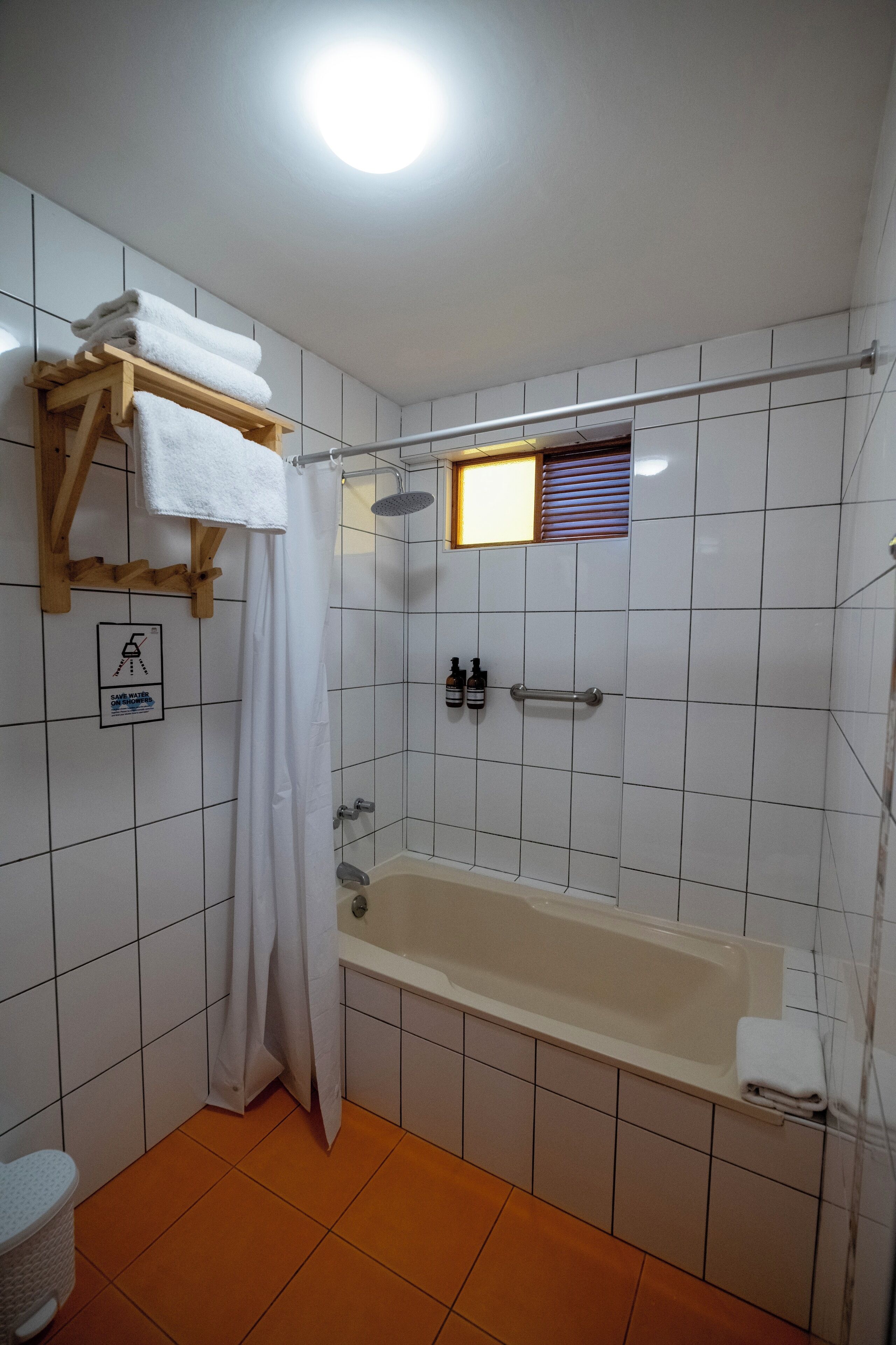 A bathroom with a bathtub, a shower, and a toilet. There is a towel rack with towels, a shower curtain, and a sign indicating a water fountain.