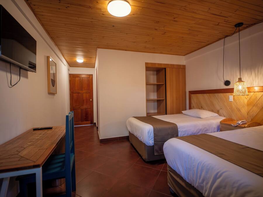 A hotel room with two beds, a wooden desk, a television, and a wooden ceiling.