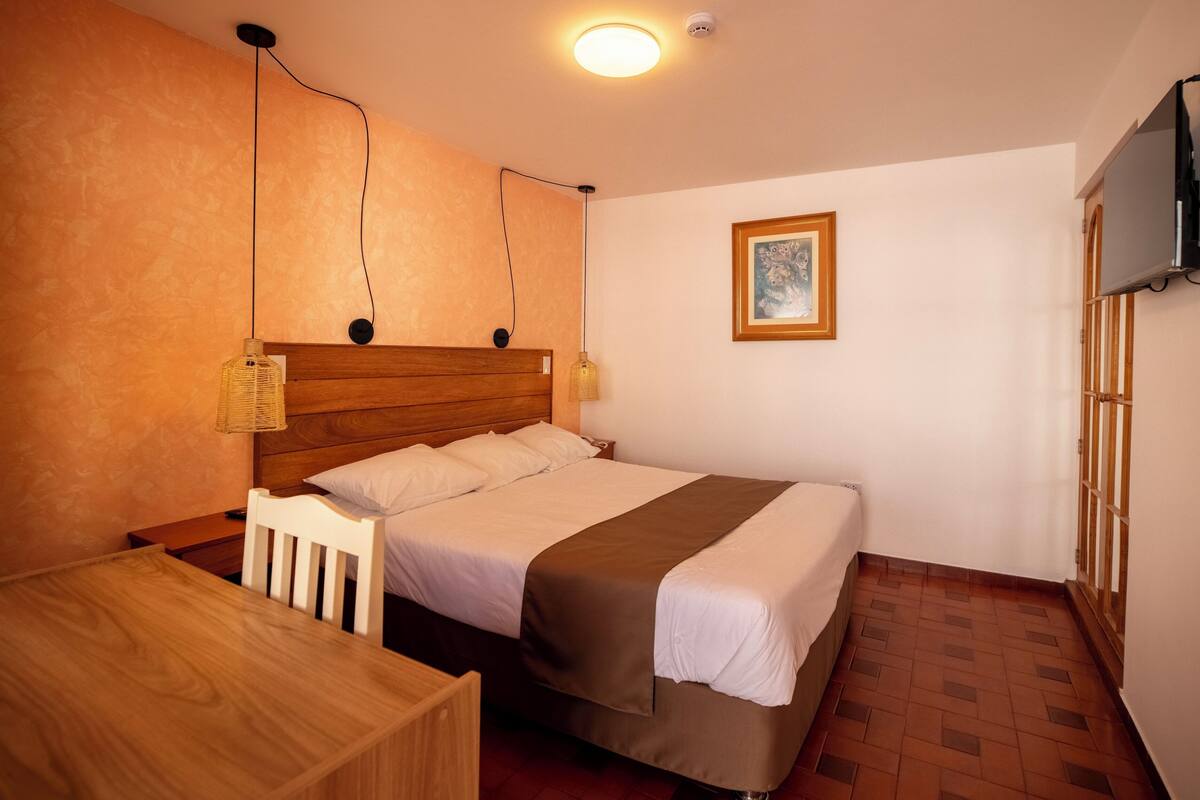 Un dormitorio con una cama de madera, una mesita de noche, una lámpara colgante y un cuadro enmarcado en la pared.