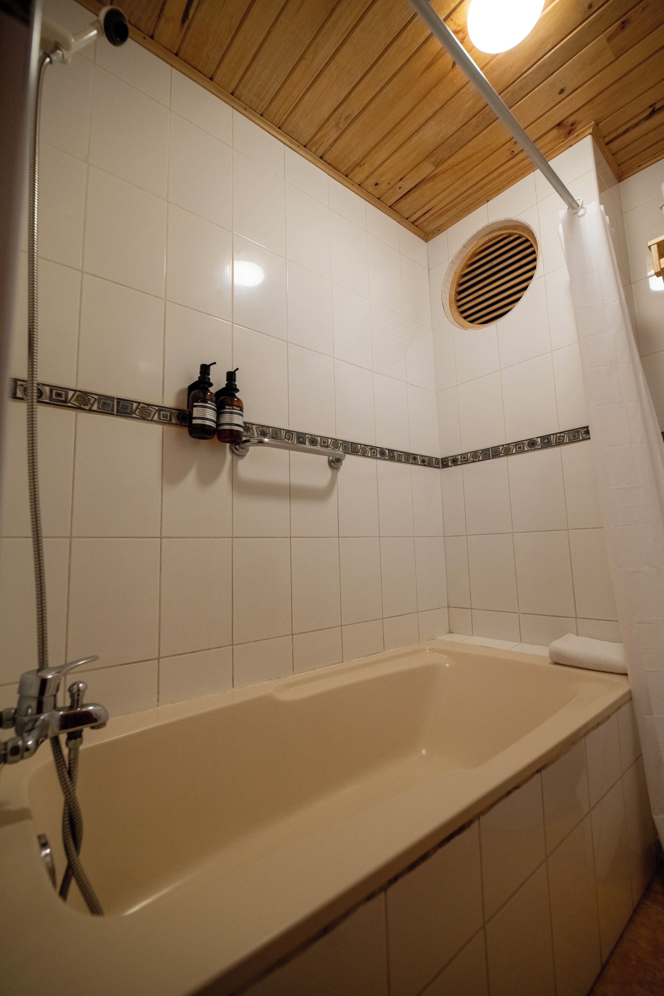 A bathroom with a bathtub, a shower, and a shelf with bottles.