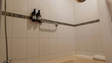A bathroom with a bathtub, a shower, and a shelf with bottles.