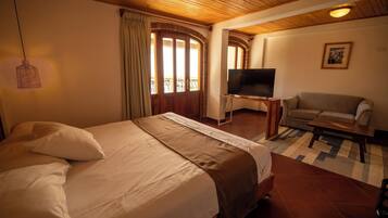 A hotel room with a large bed, a TV on a stand, a sofa, and a window with curtains.