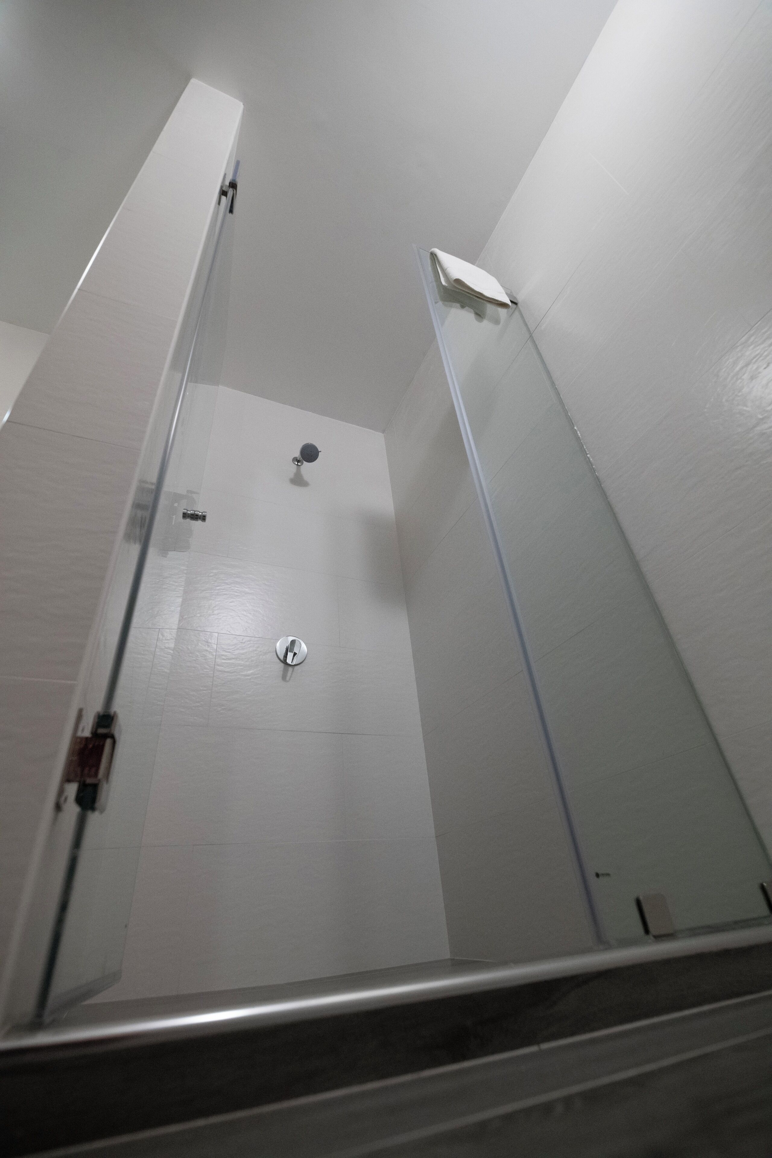 Un espace douche étroit et fermé, doté d’une porte en verre et d’un mur recouvert de carreaux blancs.