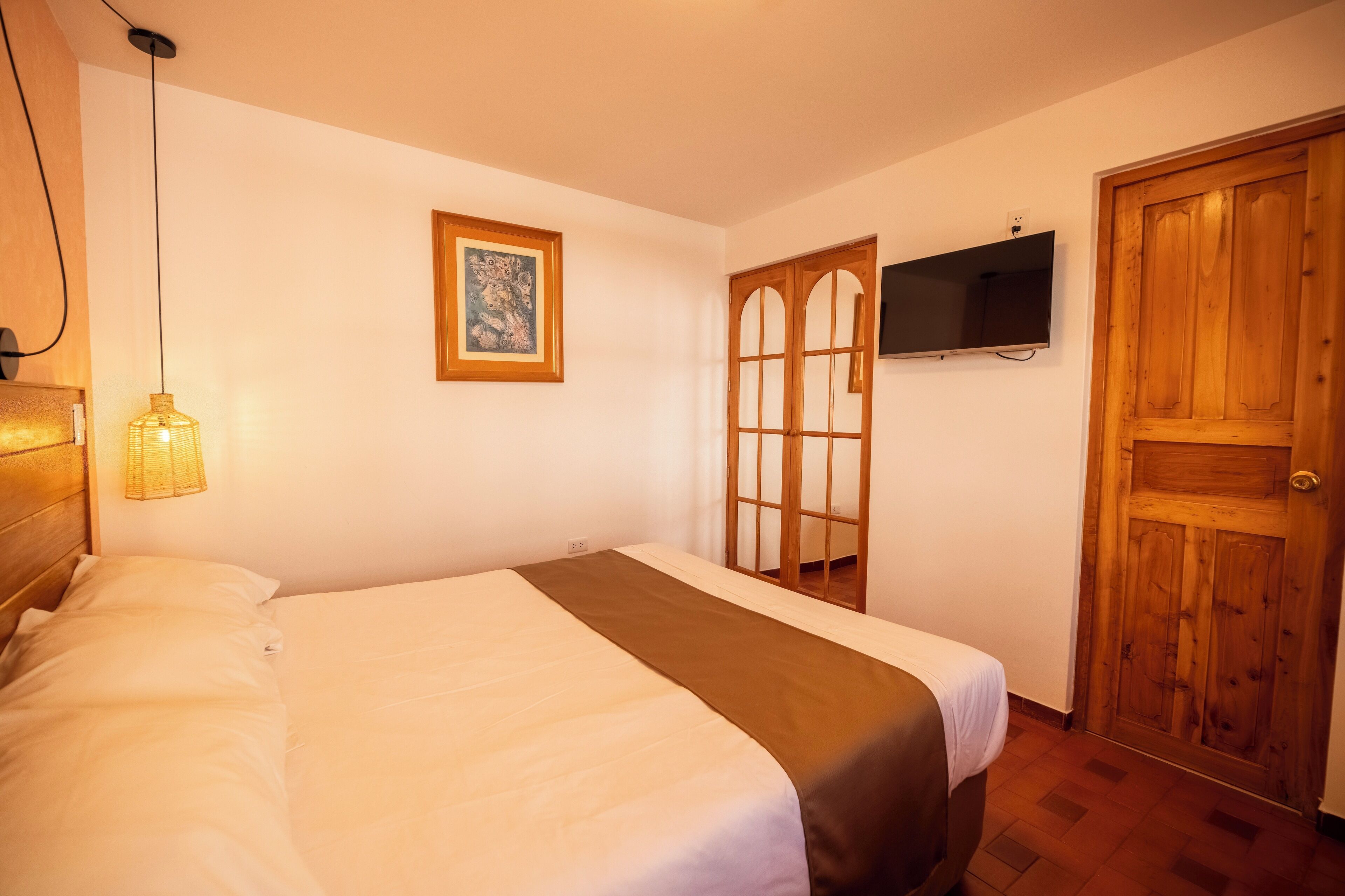 A bedroom with a bed, a television mounted on the wall, a wooden door, and a framed picture on the wall.