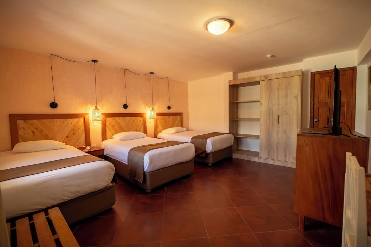 Una habitación de hotel con tres camas, cabeceros de madera y un armario empotrado.