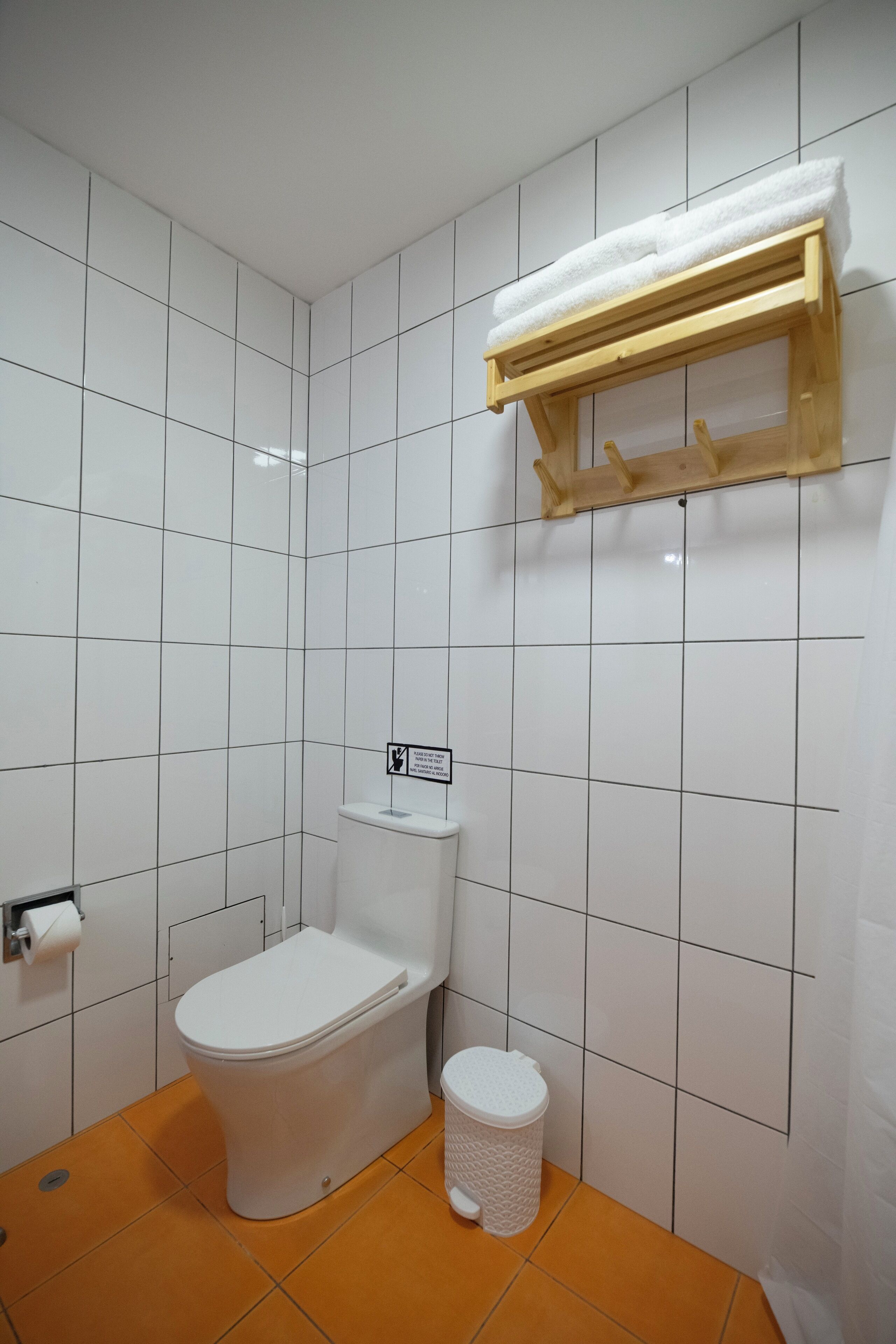 A bathroom with a toilet, a trash bin, and a shelf with a towel.
