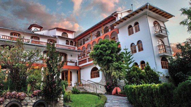 A multi-story building with a courtyard, featuring balconies, a stone pathway, and lush greenery. - San Sebastian Hotel Boutique (Huaraz)