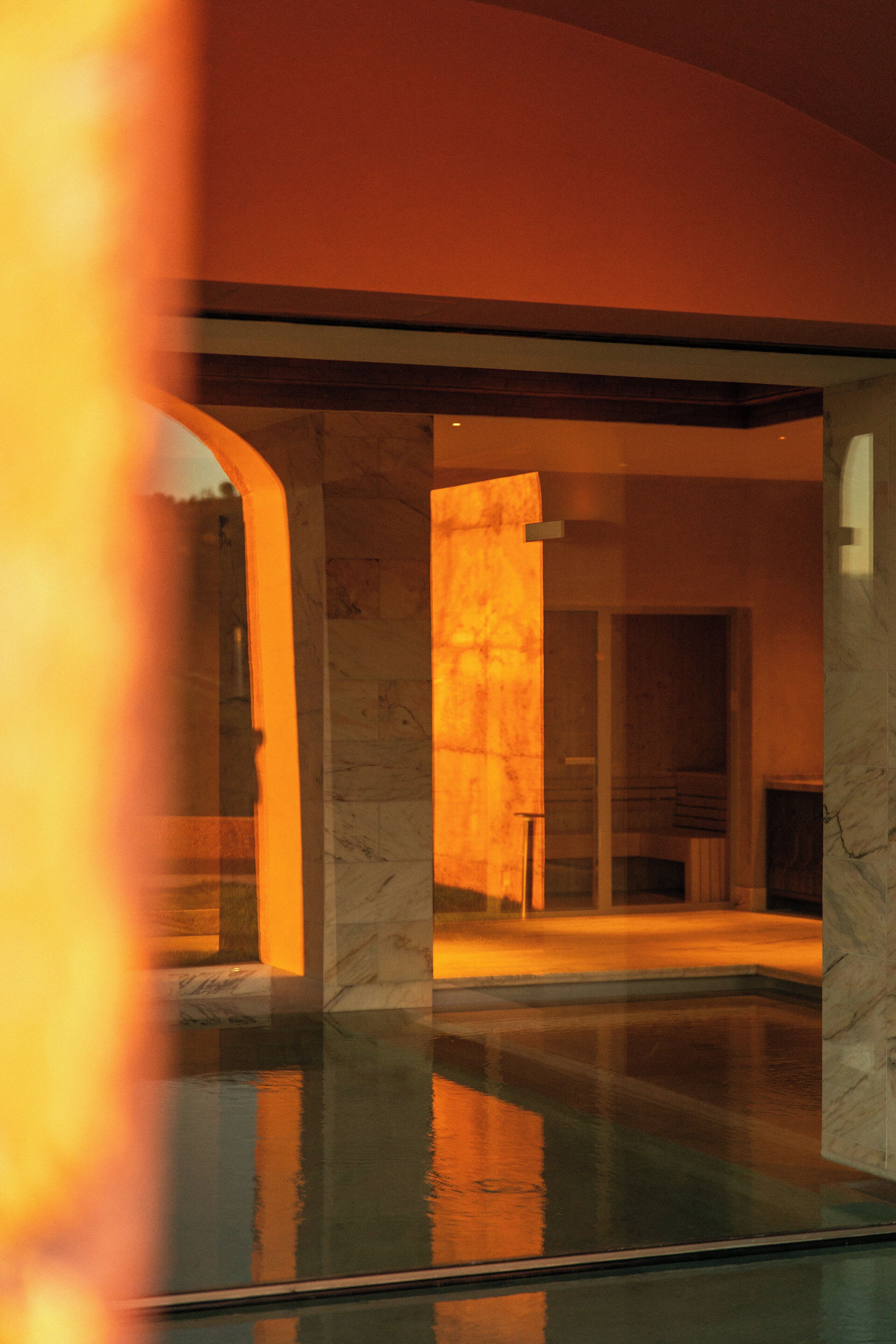 A modern interior with a glass pool, marble columns, and warm lighting.