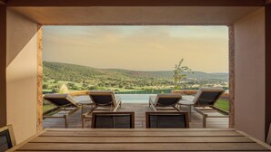 Una terraza con cuatro tumbonas que da a una piscina y una vista panorámica de colinas y vegetación.