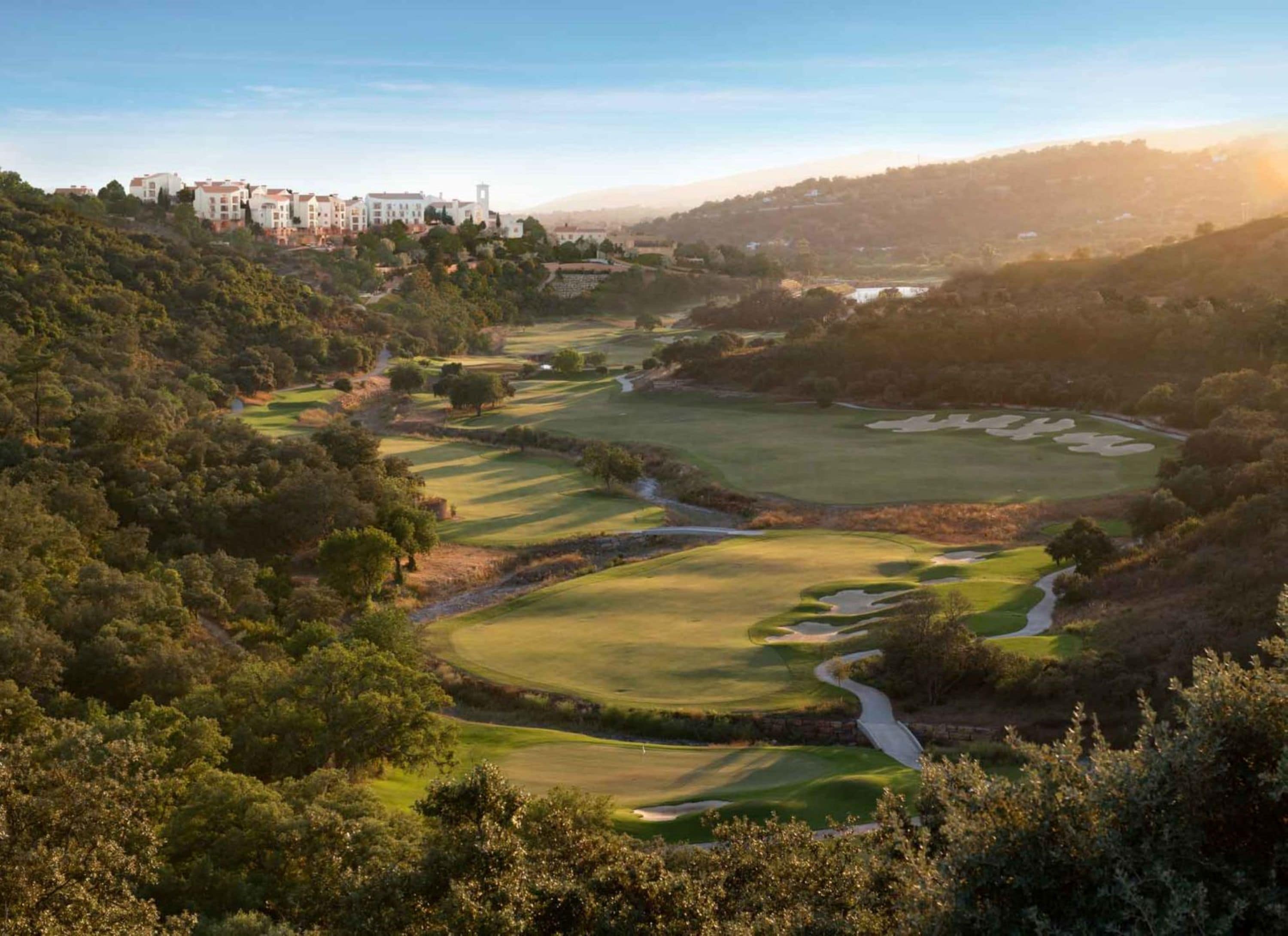 A golf course with a winding path, surrounded by dense trees and a building in the background.