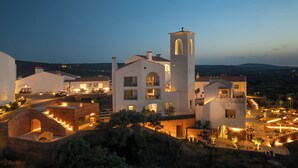 Un hotel moderno con una torre destacada, varias edificaciones conectadas y un área exterior ajardinada con mobiliario.