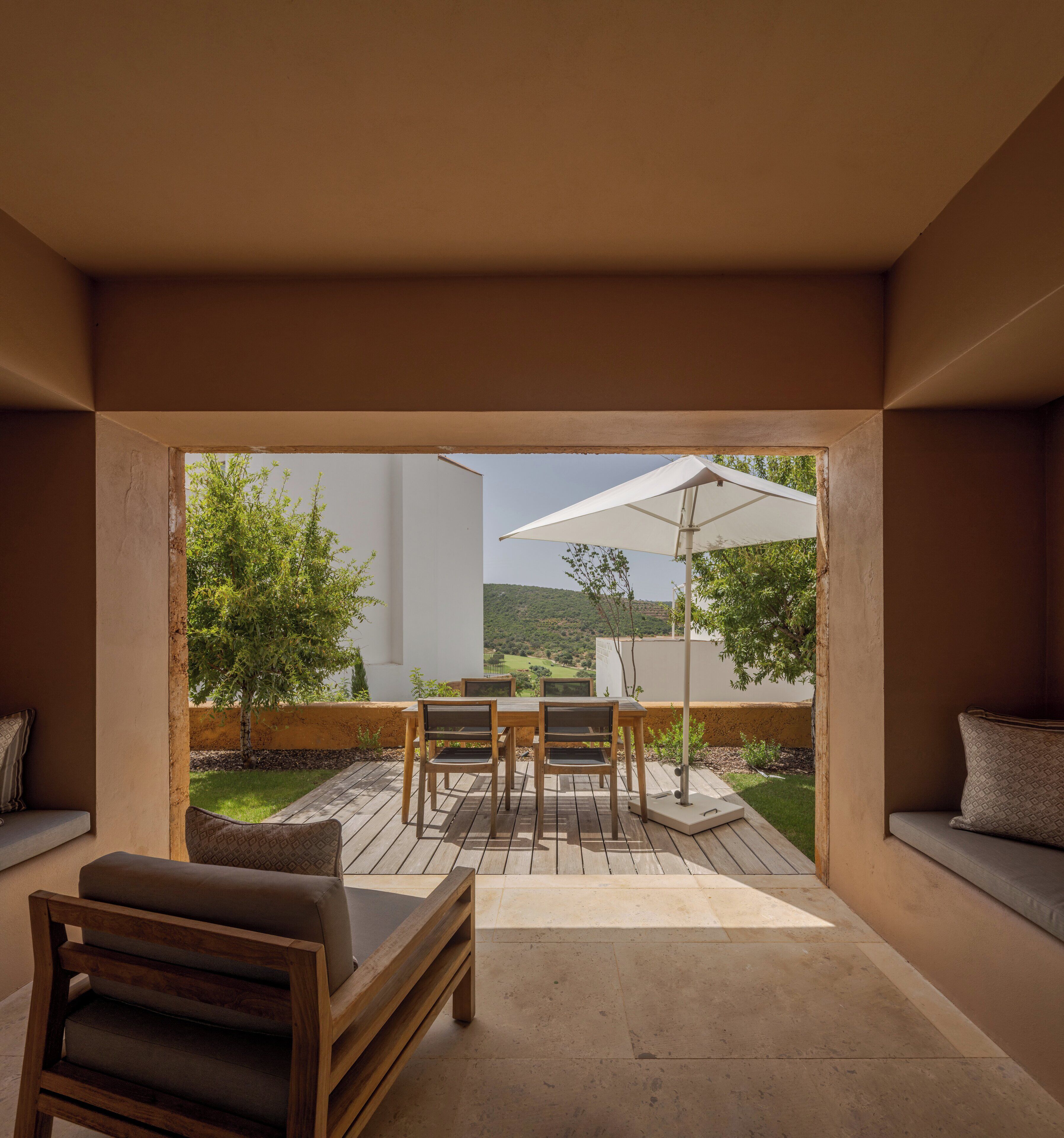 Un patio con mesa y sillas de madera, un paraguas y vistas a un paisaje verde.