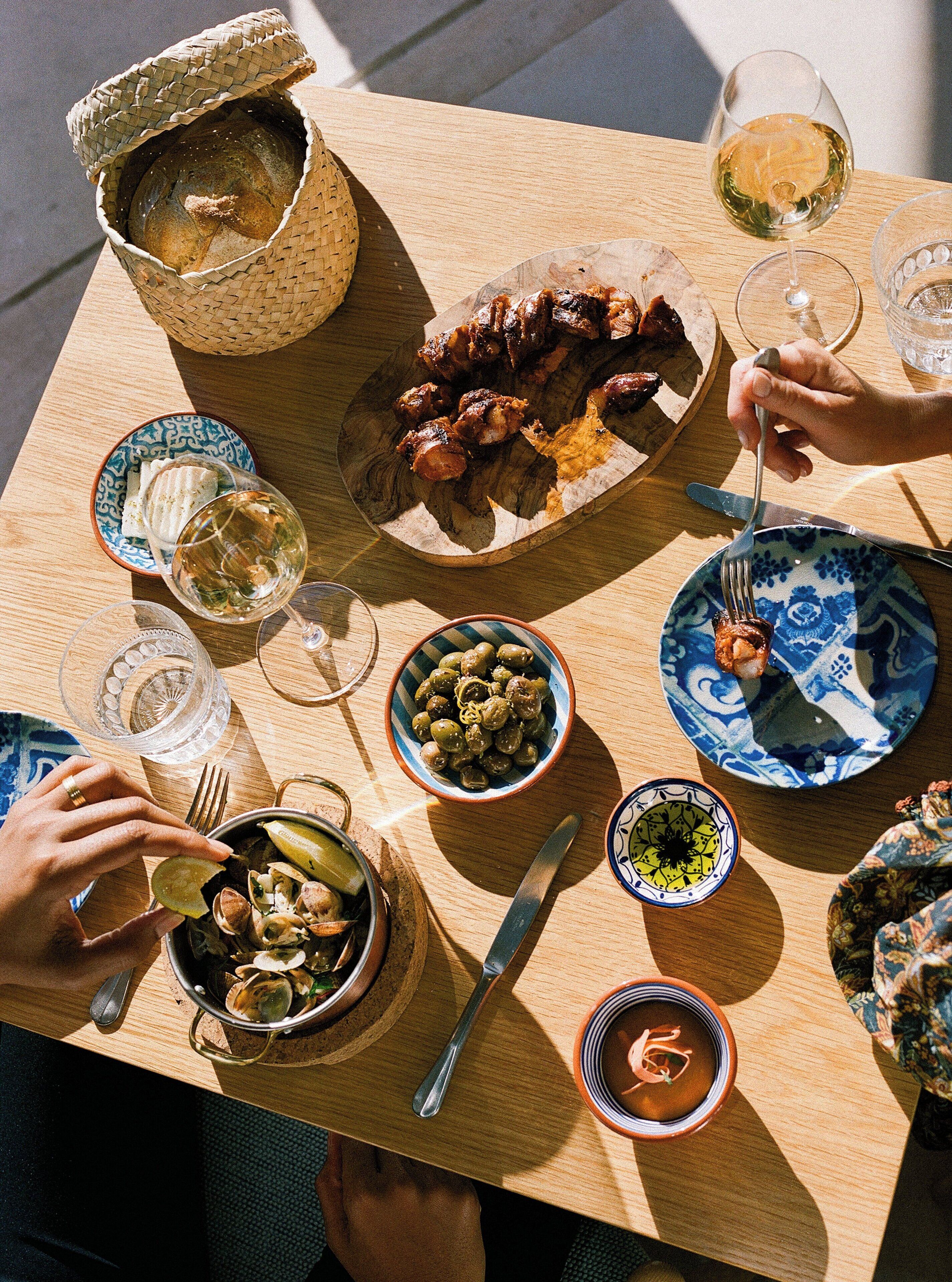 Una mesa de madera con varios platos, incluyendo aceitunas, almejas y carne, junto con varias copas de vino.