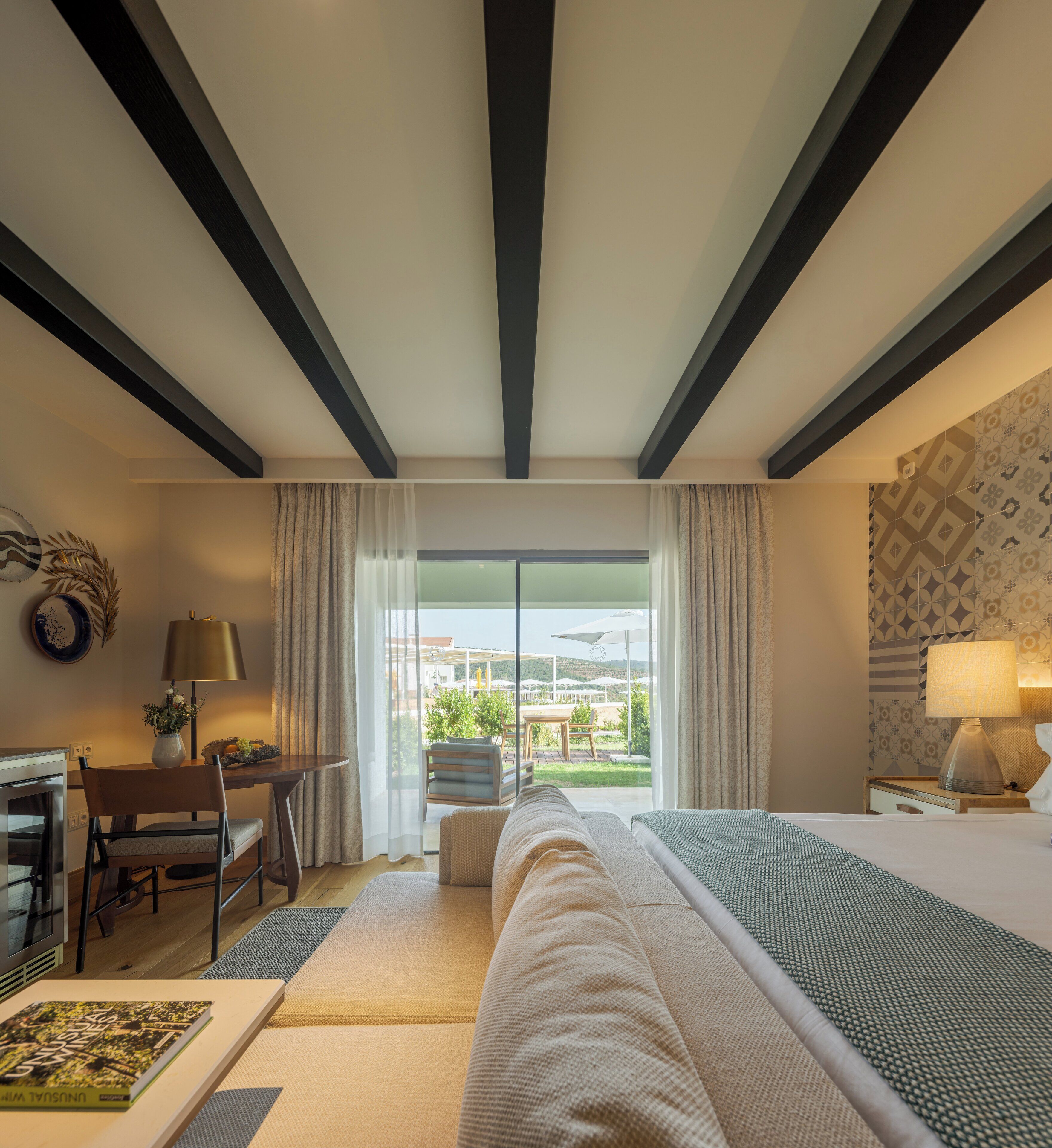 A hotel room with a bed, a desk, a chair, a lamp, and a view of the outdoors.