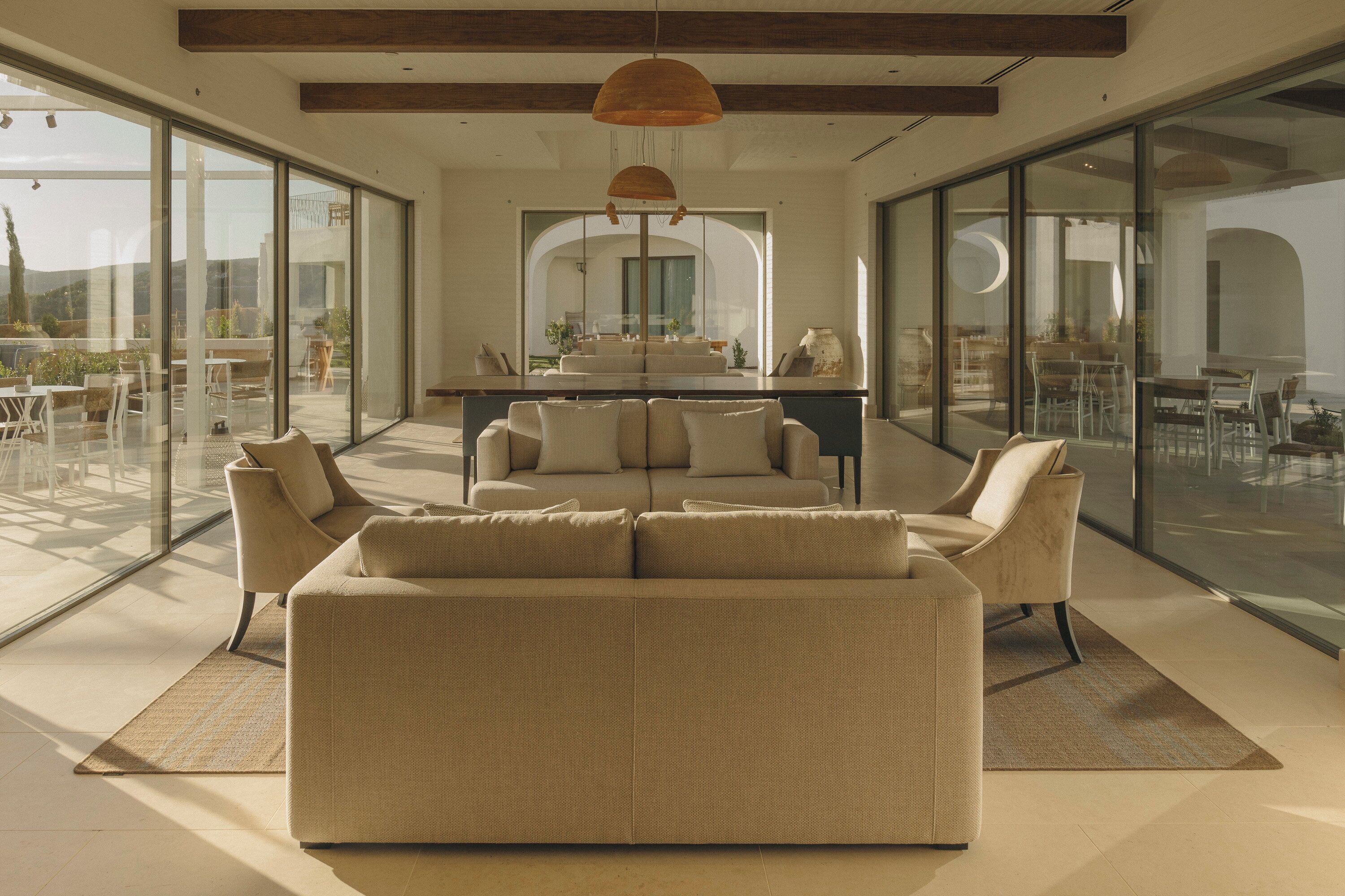 Un salon moderne avec un grand canapé beige, un coin repas doté d’une table ronde et de grandes portes vitrées donnant sur une terrasse extérieure.