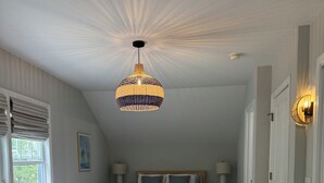 Een slaapkamer met een bed, een stoel, een nachtkastje, een lamp, een hanglamp en een deur.