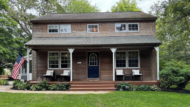 Een huis met twee verdiepingen, een veranda, een blauwe deur en een kleine Amerikaanse vlag.