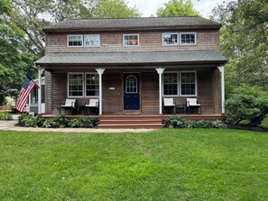 Una casa a due piani con un portico, una porta blu e una piccola bandiera americana.