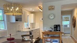 Een moderne keuken met witte kastjes, een eethoek met een houten tafel en stoelen, een koffiezetapparaat en een klok aan de muur.