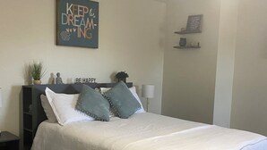 A neatly made bed with a white comforter and two pillows, a bedside table with a lamp, a small shelf with decorative items, and a motivational poster on the wall. - Charming 4-bedroom house with AC and WiFi in amazing Cedar Hill (Cedar Hill)