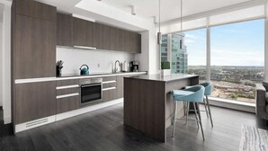 A modern kitchen with dark wood cabinets, a central island, and a large window offering a city view. - Midnight Rose-Your Elevated Stay! (Calgary)