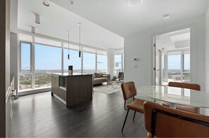 A spacious living area with a large glass table, a sofa, and a kitchen island. - Midnight Rose-Your Elevated Stay! (Calgary)