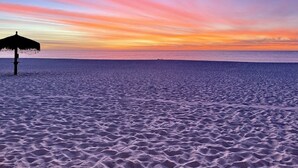 A beach with a thatched umbrella and a calm sea at sunset.
