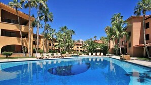 A swimming pool surrounded by palm trees and a building with balconies.