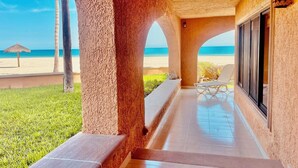 A covered outdoor area with a view of the beach, a palm tree, and a lounge chair.