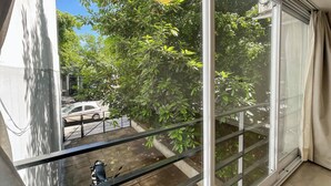 A balcony with a view of a parked car and a tree.