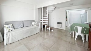 A modern living room with a grey sofa, a dining table with chairs, and a staircase leading to another level.