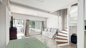 A hotel room with a bed, a desk, a chair, a staircase, and a view of the outside.