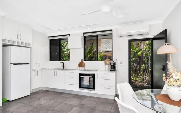A modern kitchen with white cabinetry, a built-in oven, a sink, and a dining area with a glass table and chairs.