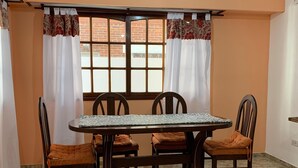 Ein Essbereich mit Tisch und vier Stühlen, einer Hängeleuchte und einem Fenster mit Vorhängen.